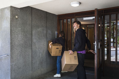 Couple entering building carrying boxes