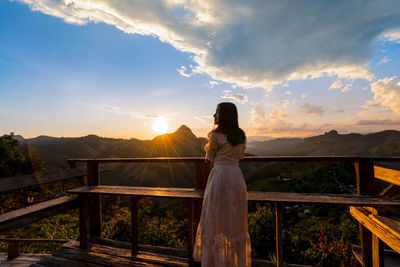 Rear view of woman looking at sea against sky during sunset