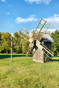 Wooden old windmill on a green lawn against a blue sky on a sunny day.