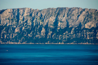 Scenic view of rock mountain by sea against clear blue sky