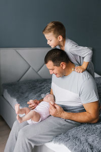 Father holding a newborn daughter looks at her on the bed. the girl's brother also looks