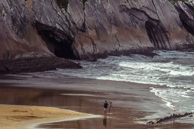 Man photographing at beach against rocky mountain