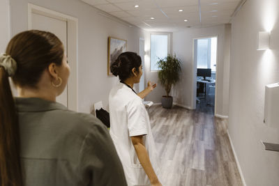 Female healthcare worker escorting patient towards examination room at healthcare center