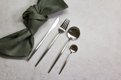 Knife, spoons and fork with green textile napkin on grey stone background. table setting. top view.