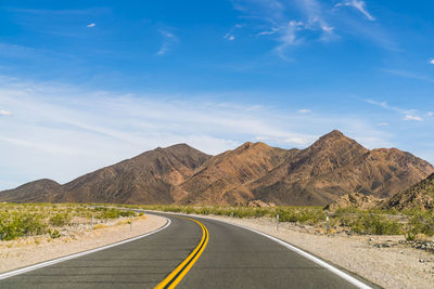 Empty road by mountains against sky