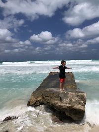 Full length of man on rock at beach against sky