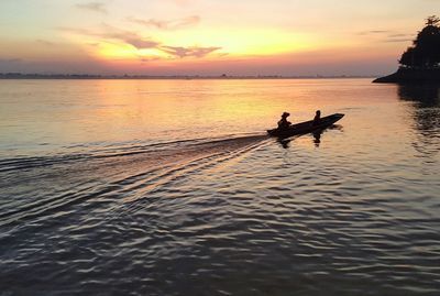 Silhouette people on sea against sky during sunset