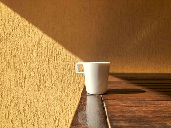 Minimalistic shot of a white cup sitting in the bright sunlight on a wooden table