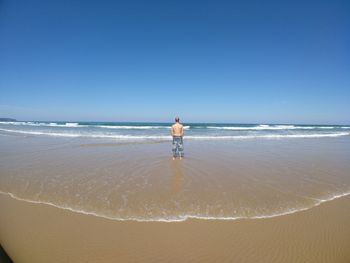 Rear view of man standing on beach against clear blue sky