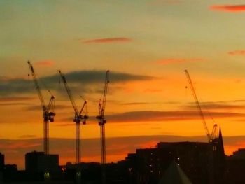 Silhouette of cranes against dramatic sky during sunset