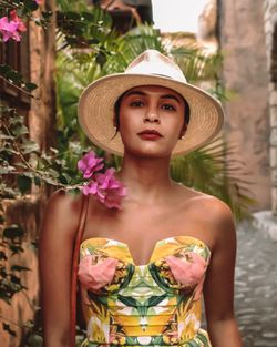 Portrait of young woman wearing hat standing against plants