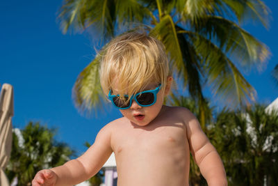 Shirtless boy standing against tree