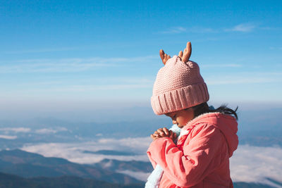 Girl praying while standing against sky during winter