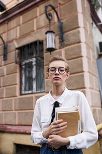 Young woman looking away while standing against built structure