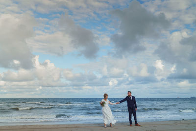 Full length of friends standing on beach against sky