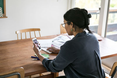 High angle view of businesswoman video calling female colleague on mobile phone in home office