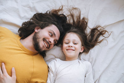 Young happy family bearded father and daughter on bed in cozy home, view from top