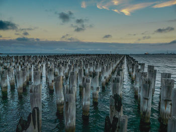 Wooden posts in sea against sky at sunset