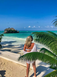 Rear view of woman standing by tree at beach