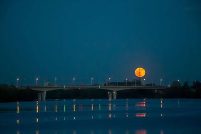 Illuminated bridge over river against sky at night