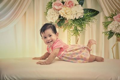 Portrait of cute baby girl lying on bed against curtain