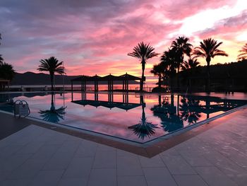 Palm trees by swimming pool against sky during sunset