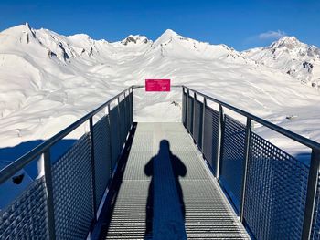 Shadow of railing on snow covered mountain against sky