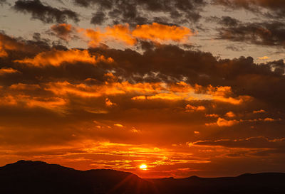 Scenic view of dramatic sky over silhouette mountains during sunset