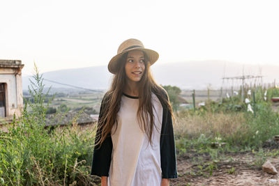 Young woman wearing hat looking away standing at farm