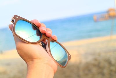 Close-up of hand holding eyeglasses against sea