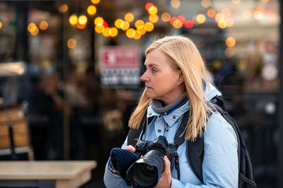 Blonde middle-aged woman with a photo camera in the evening on the city streets, lifestyle concept