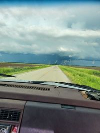 Road amidst field seen through car windshield