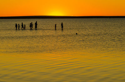 Silhouette people on beach against orange sky