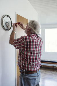 Senior man repairing sconce on white wall at home