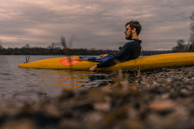 Side view of man kayaking in lake against sky