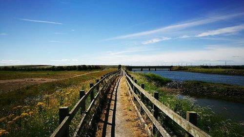 Boardwalk amidst landscape against sky during sunny day