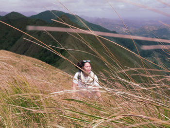 Young woman seen through plants looking away while sitting on mountain