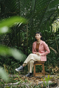 Young woman sitting on stool by tree outdoors