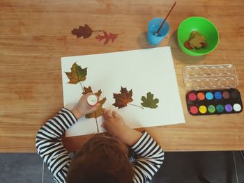 High angle view of boy sticking autumn leaves on paper