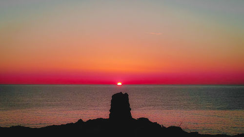Silhouette rocks on sea against romantic sky at sunset