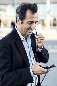 Businessman communicating through headphones while using mobile phone on street