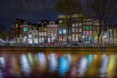 Light reflecting on river against illuminated buildings at night