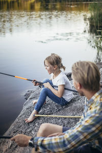 Smiling daughter enjoying fishing with father at lake