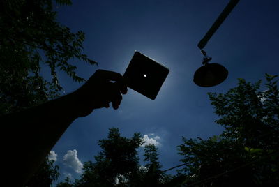 Low angle view of hand holding smart phone against sky