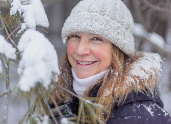 Portrait of smiling mature woman standing by plant during winter in forest