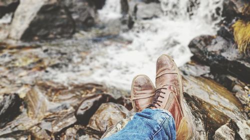 Low section of man wearing shoes on rocks at riverbank