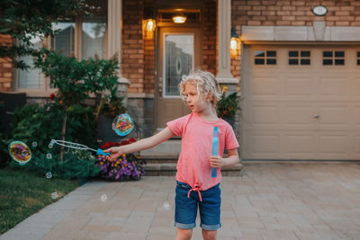 Girl blowing soap bubbles on home front yard. child seasonal summer activity for children.