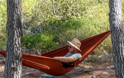 Side view of man relaxing in hammock, using laptop computer