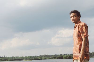 Young man looking away while standing against sky