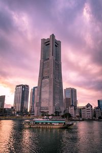 Modern buildings by river against sky during sunset